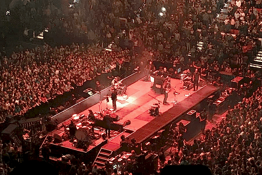 Photo of Coliseum venue filled with an audience listening to music. Musicians on the stage.